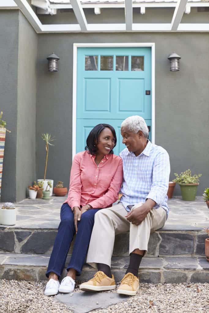 senior-couple-sit-on-steps-outside-their-house-vertical